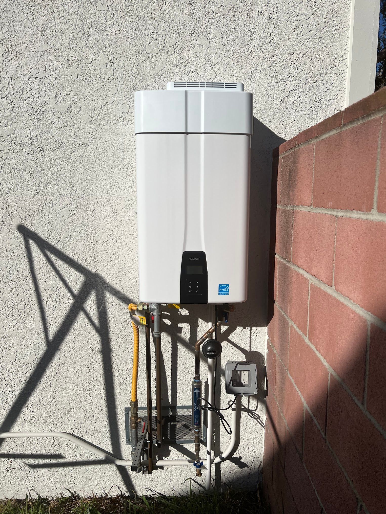 A white water heater is mounted on the side of a brick wall.