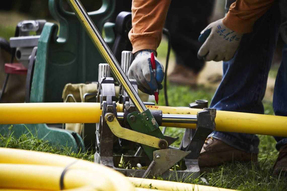 A man is working on a yellow pipe with a machine.