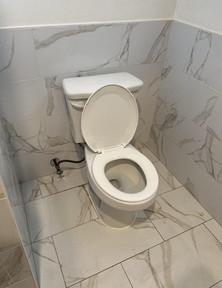 A toilet is sitting in a bathroom with marble tiles.