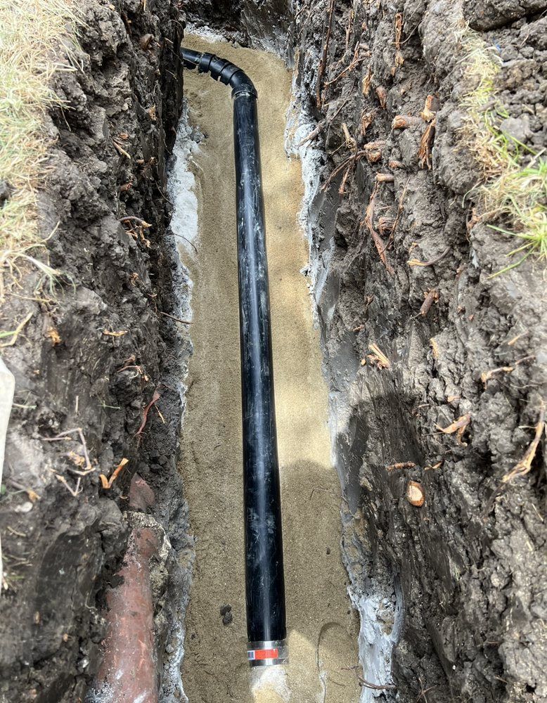 A black pipe is laying in the dirt in a trench.