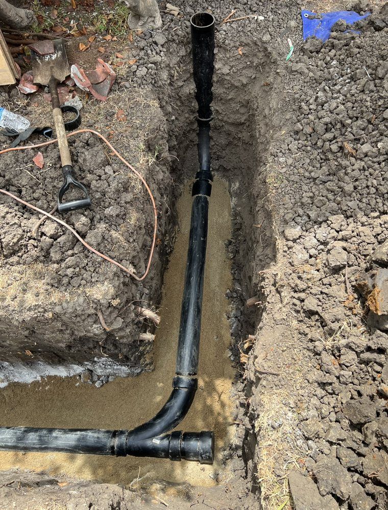A black pipe is being installed in a hole in the ground.