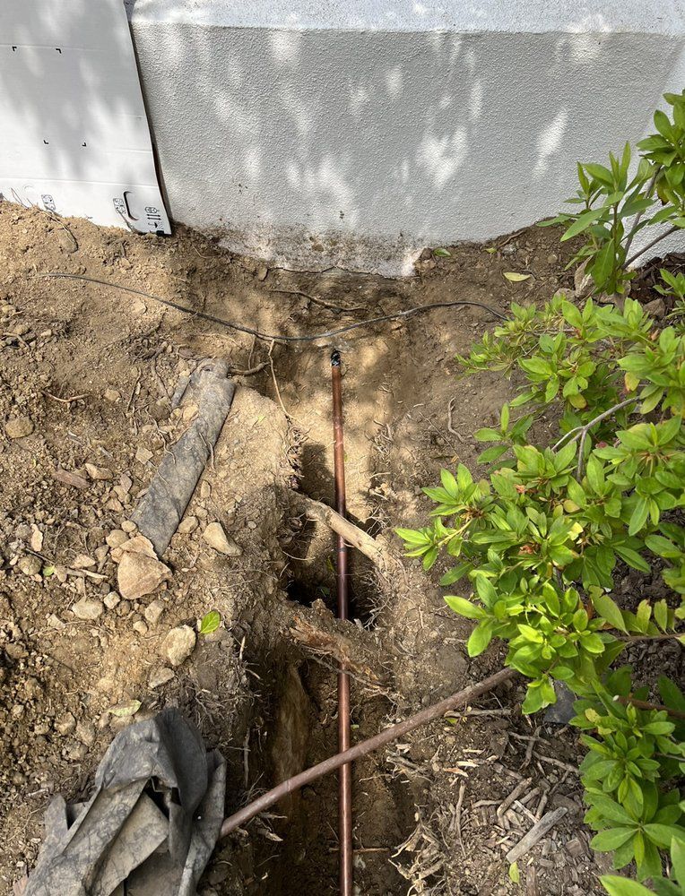 A copper pipe is being installed in the ground next to a house.