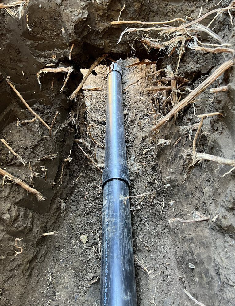 A black pipe is laying in the dirt in a hole.