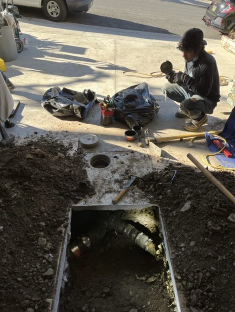 A man is kneeling in the dirt working on a pipe.