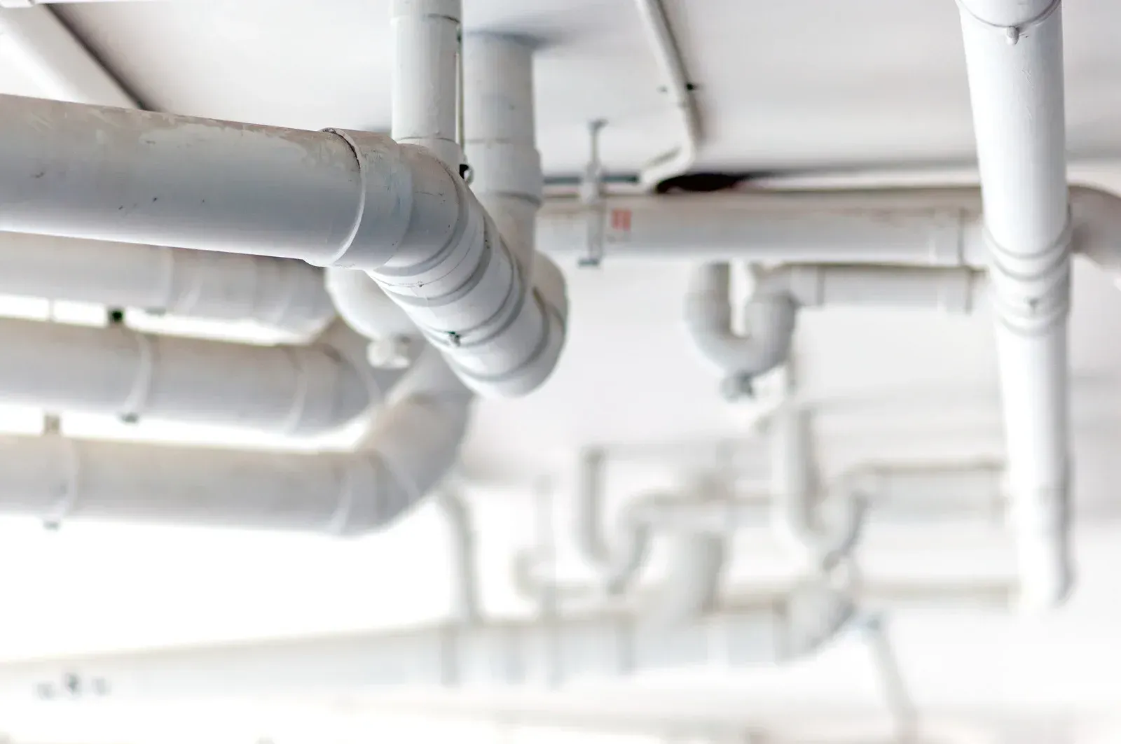 A bunch of white pipes are hanging from the ceiling of a building.