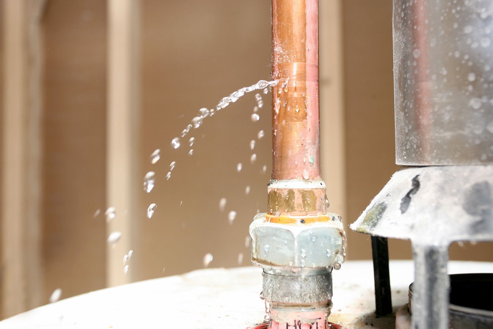 Leaking copper pipe spraying water onto a white surface indoors