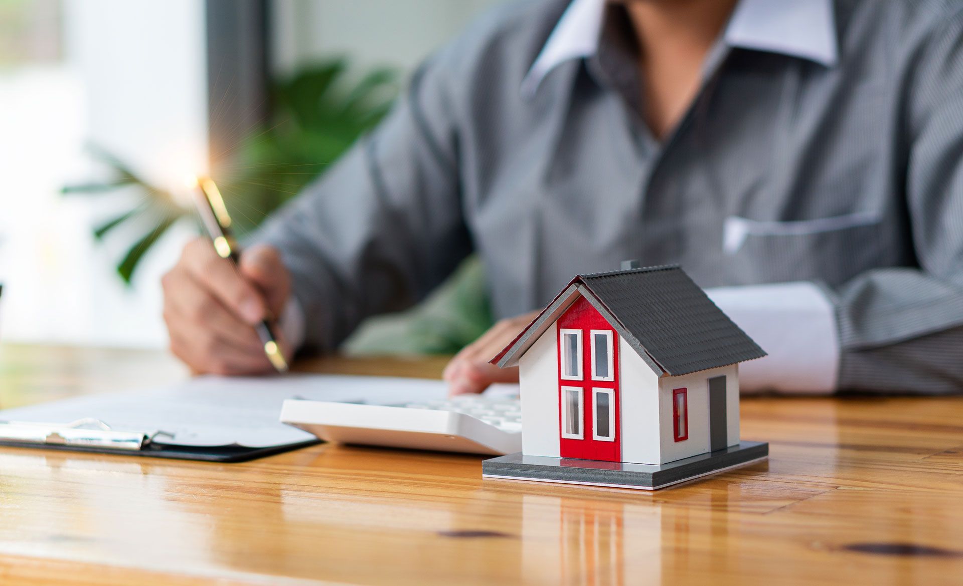 Person calculating finances with a model house on a wooden table.
