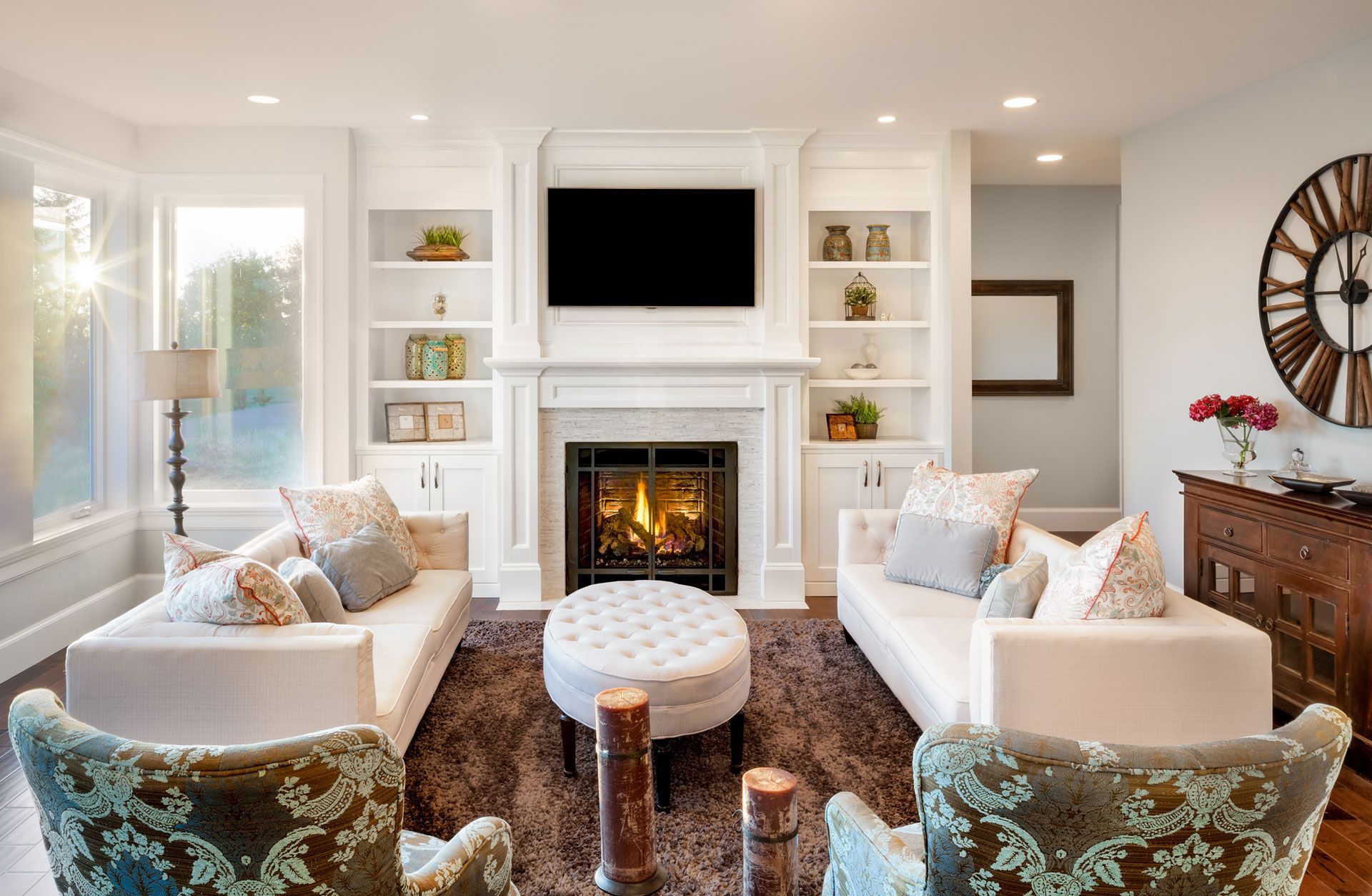 Living room with fireplace, white couches, bookshelves, TV, and large clock.