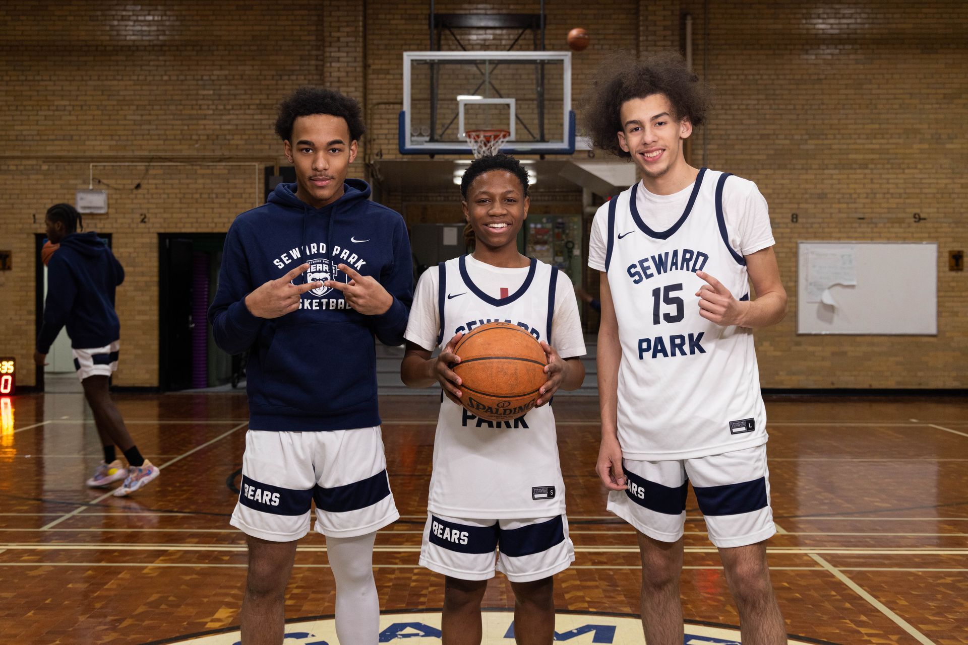 Three student basketball players pose in a gym.