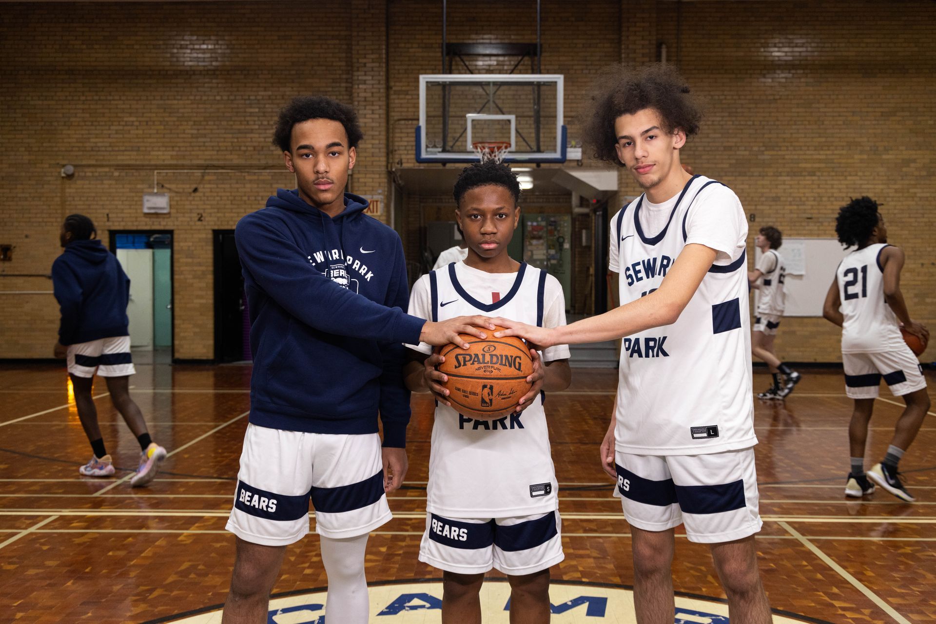 Three student basketball players holding a basketball while others run drills in the background