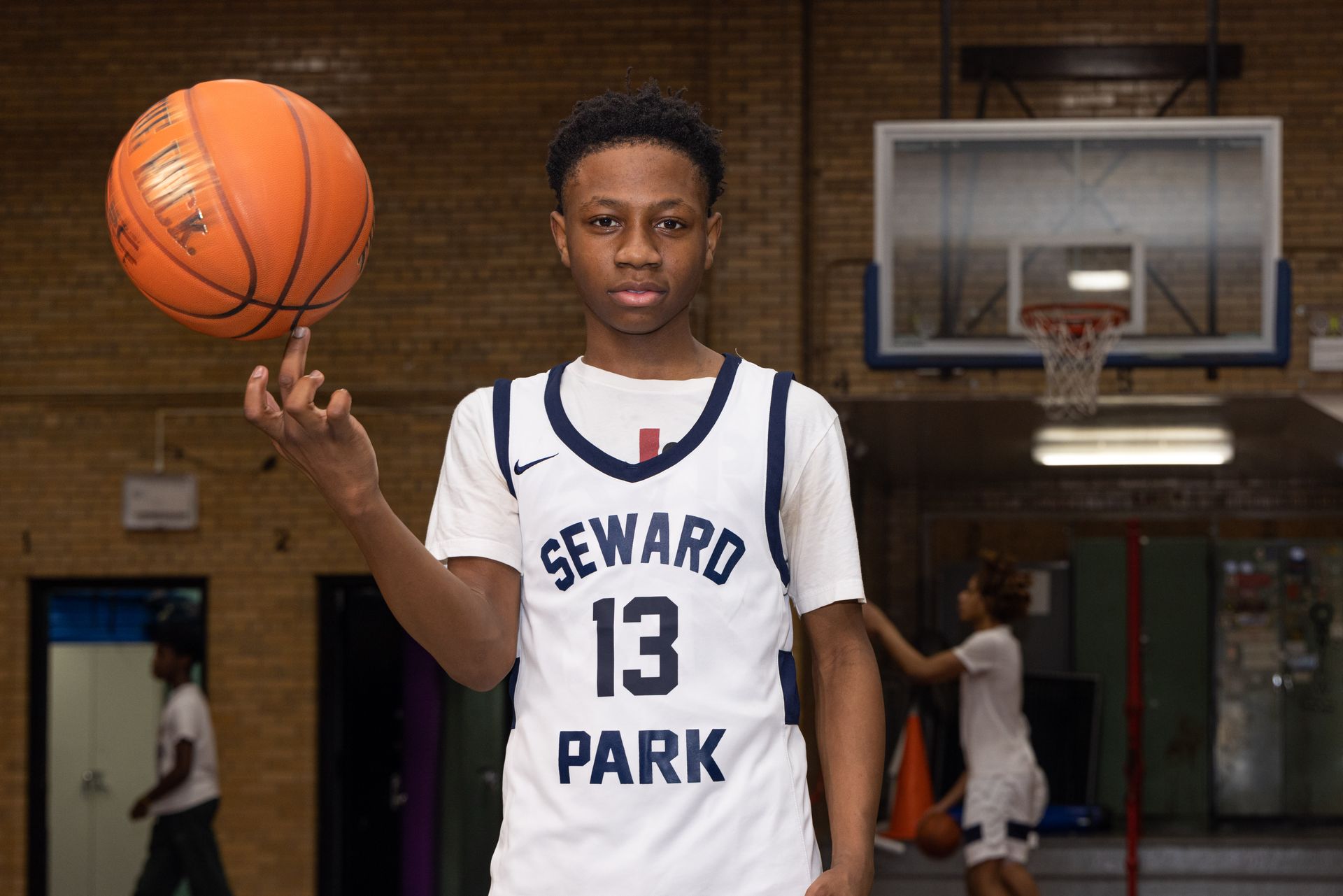 Student basketball player balancing a ball on his finger while other players run drills.