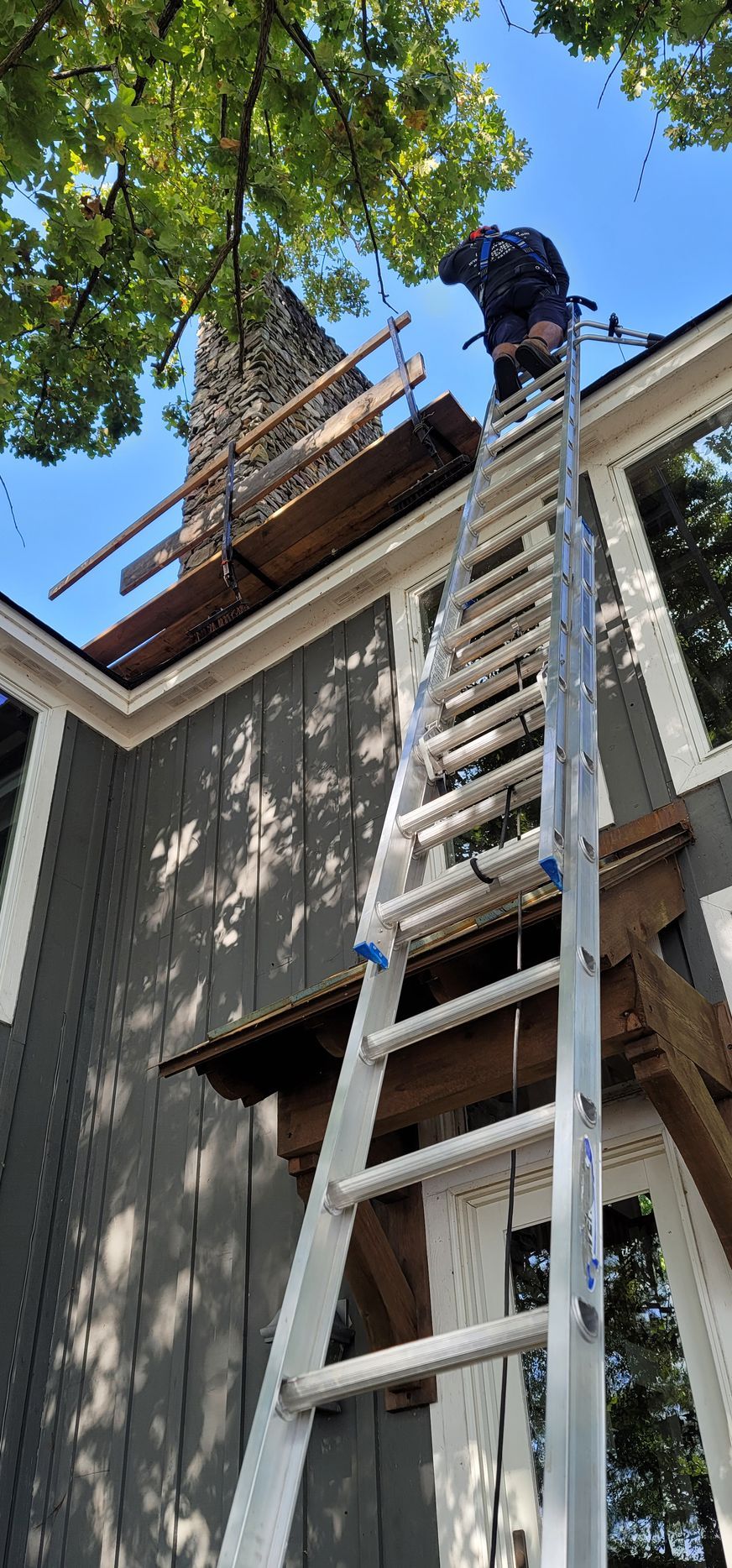 A man is standing on a ladder on the roof of a house.