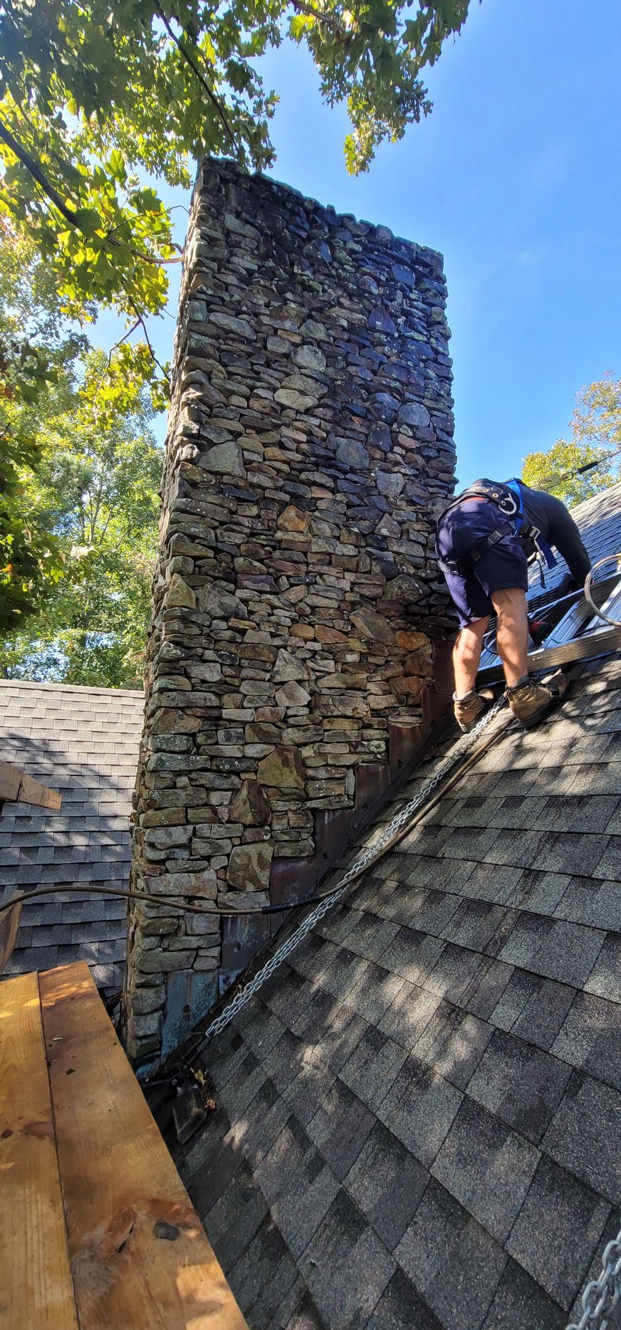 A man is standing on top of a roof next to a stone chimney.