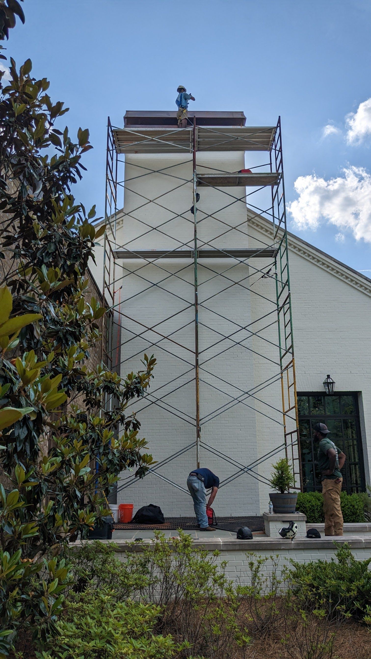 A man is standing on a scaffolding in front of a white house.