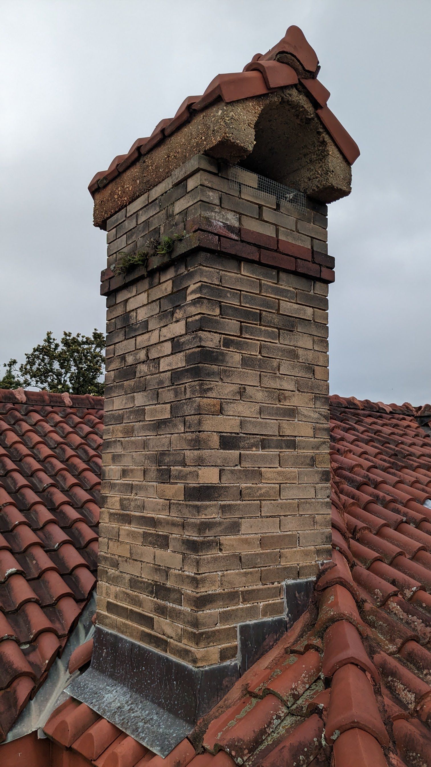 A brick chimney on top of a red tiled roof.