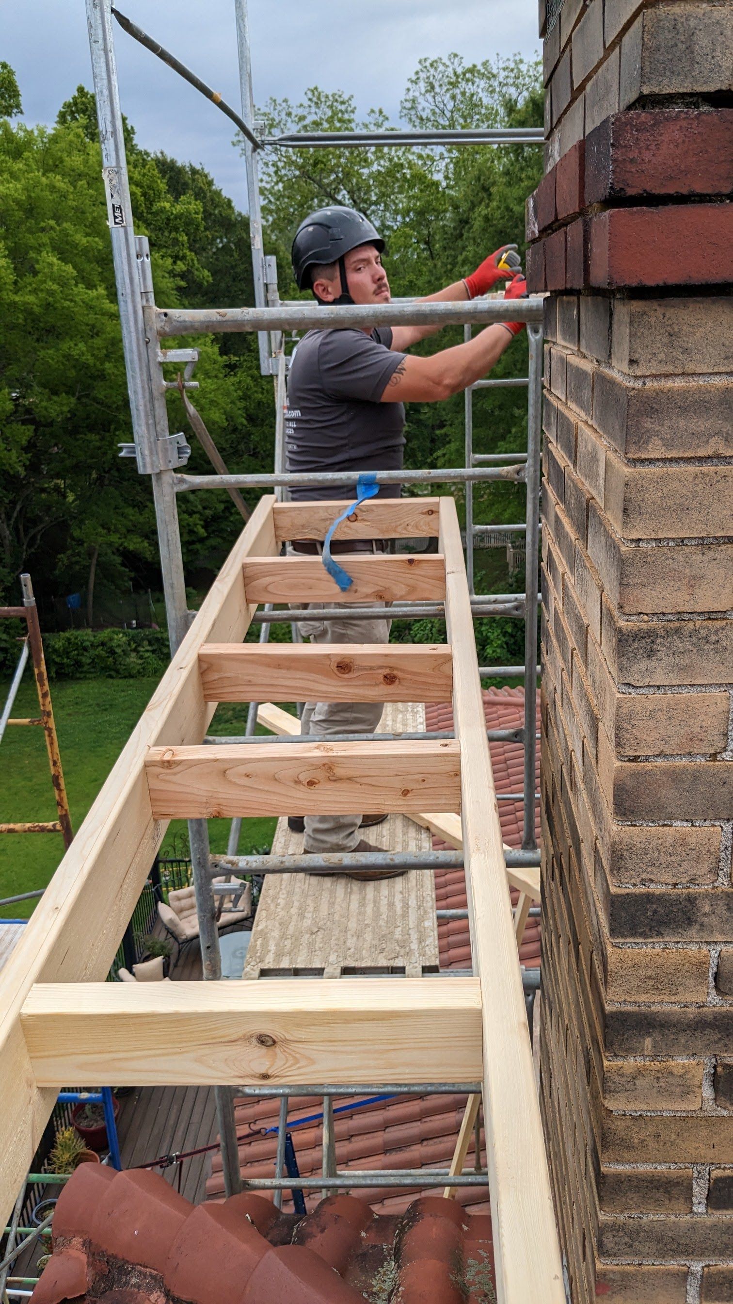 A man is standing on a wooden ladder next to a brick wall.