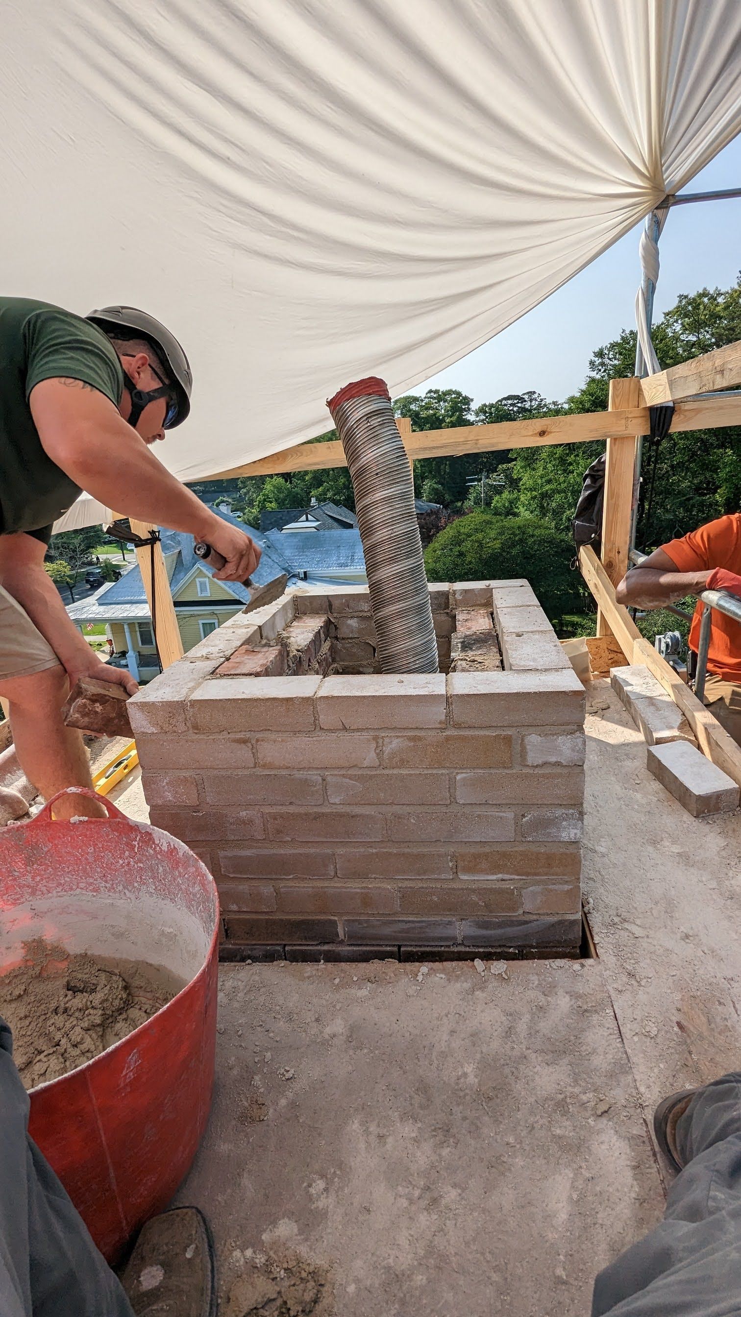 A man is working on a brick wall under a canopy.