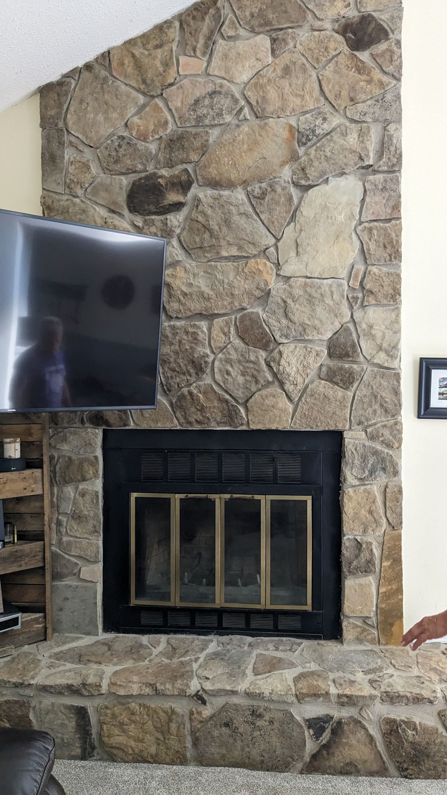 A living room with a stone fireplace and a flat screen tv.