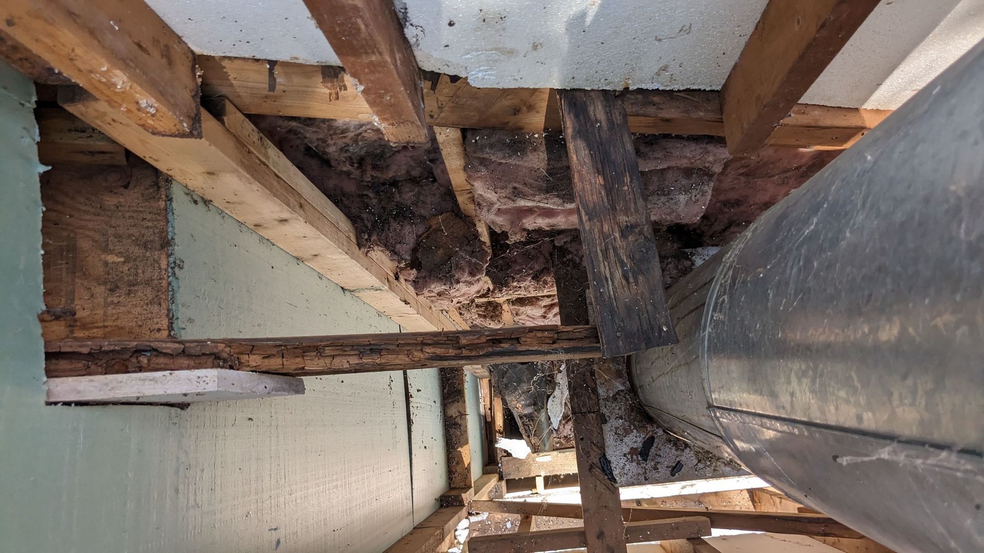 The ceiling of a building with wooden beams and a metal pipe.