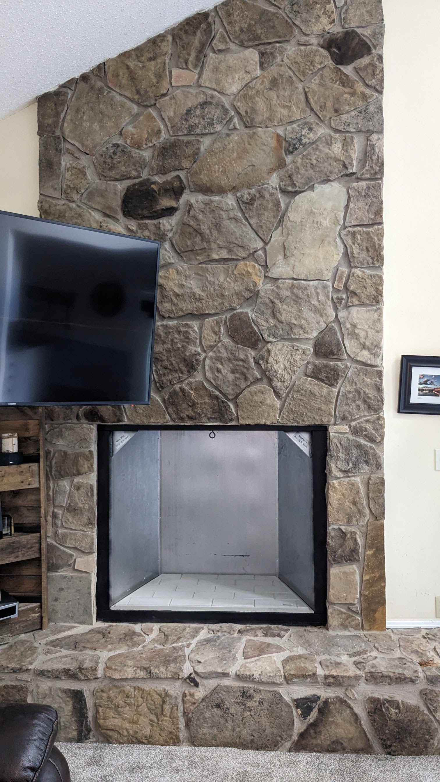 A living room with a stone fireplace and a flat screen tv.