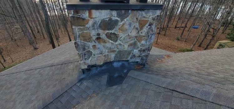 A stone chimney on top of a roof in the woods.