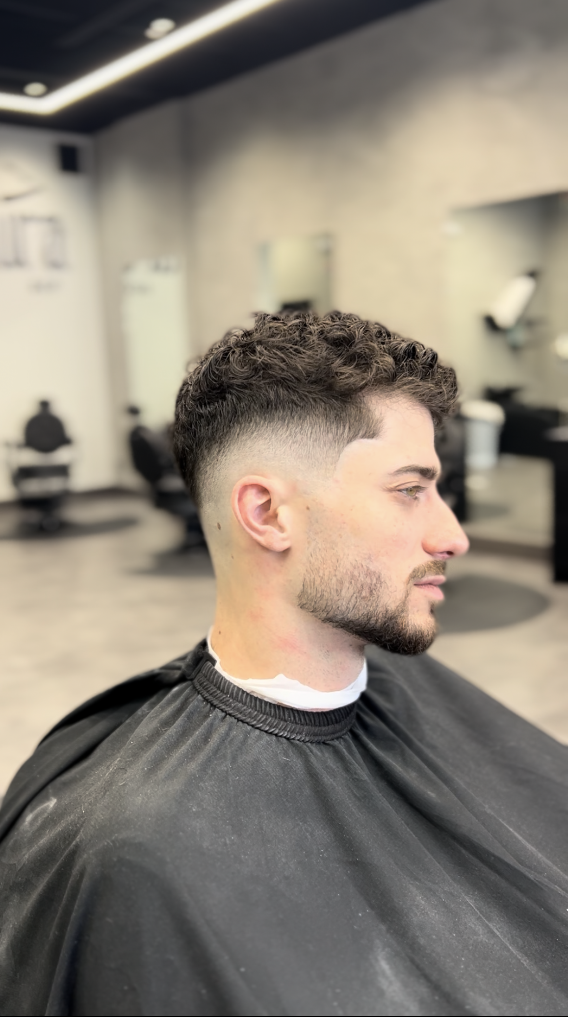 Man with a faded haircut in a barber shop, wearing a black cape.