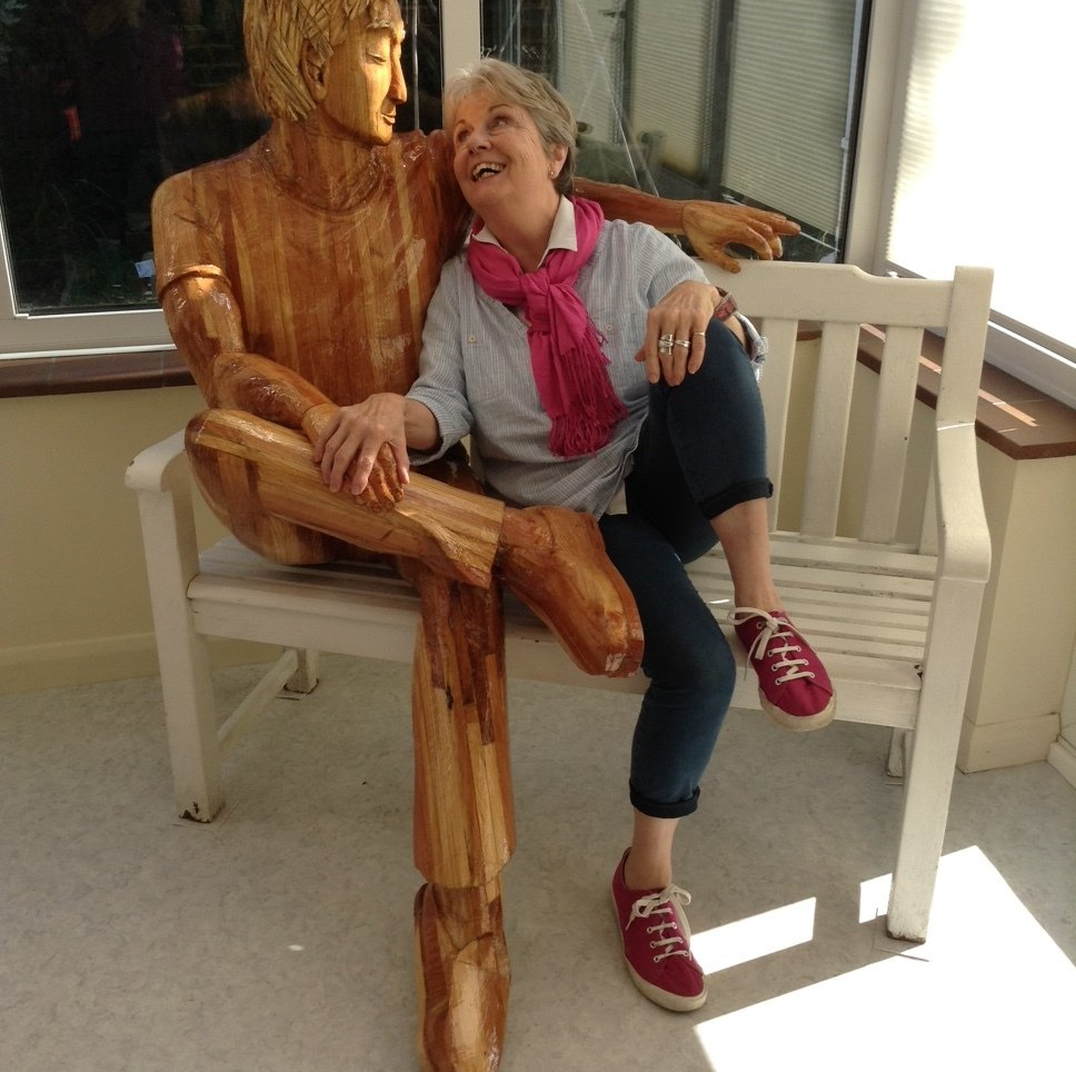 Wooden sculpture on a bench sitting with a human woman.