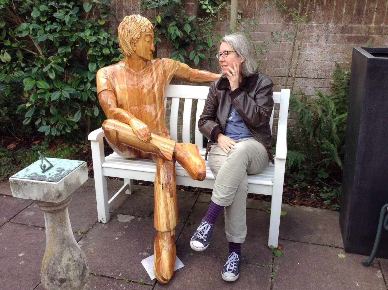 A wooden garden statue sitting with a real British woman