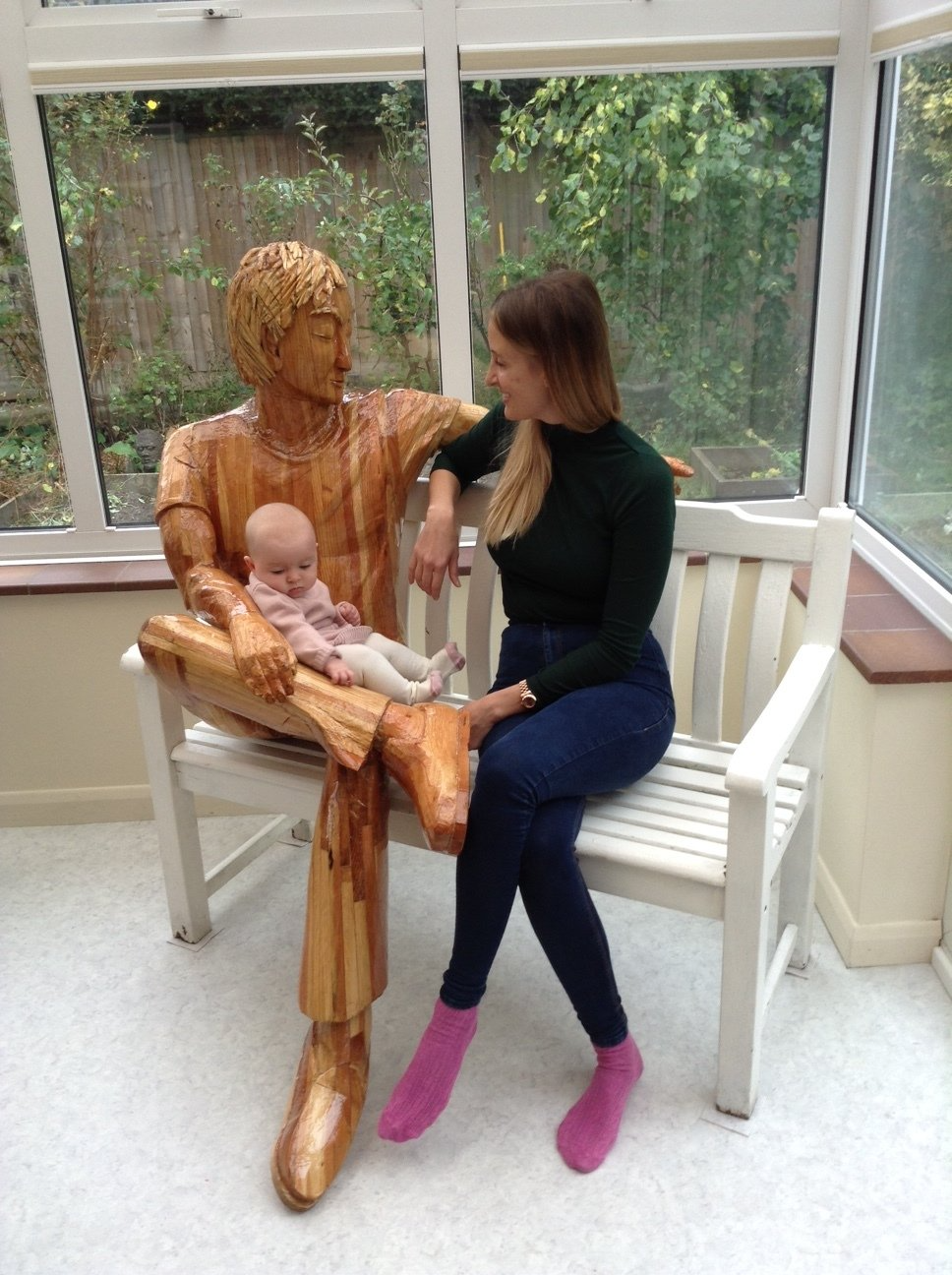 Mother and child sitting with a wooden sculpture of a man