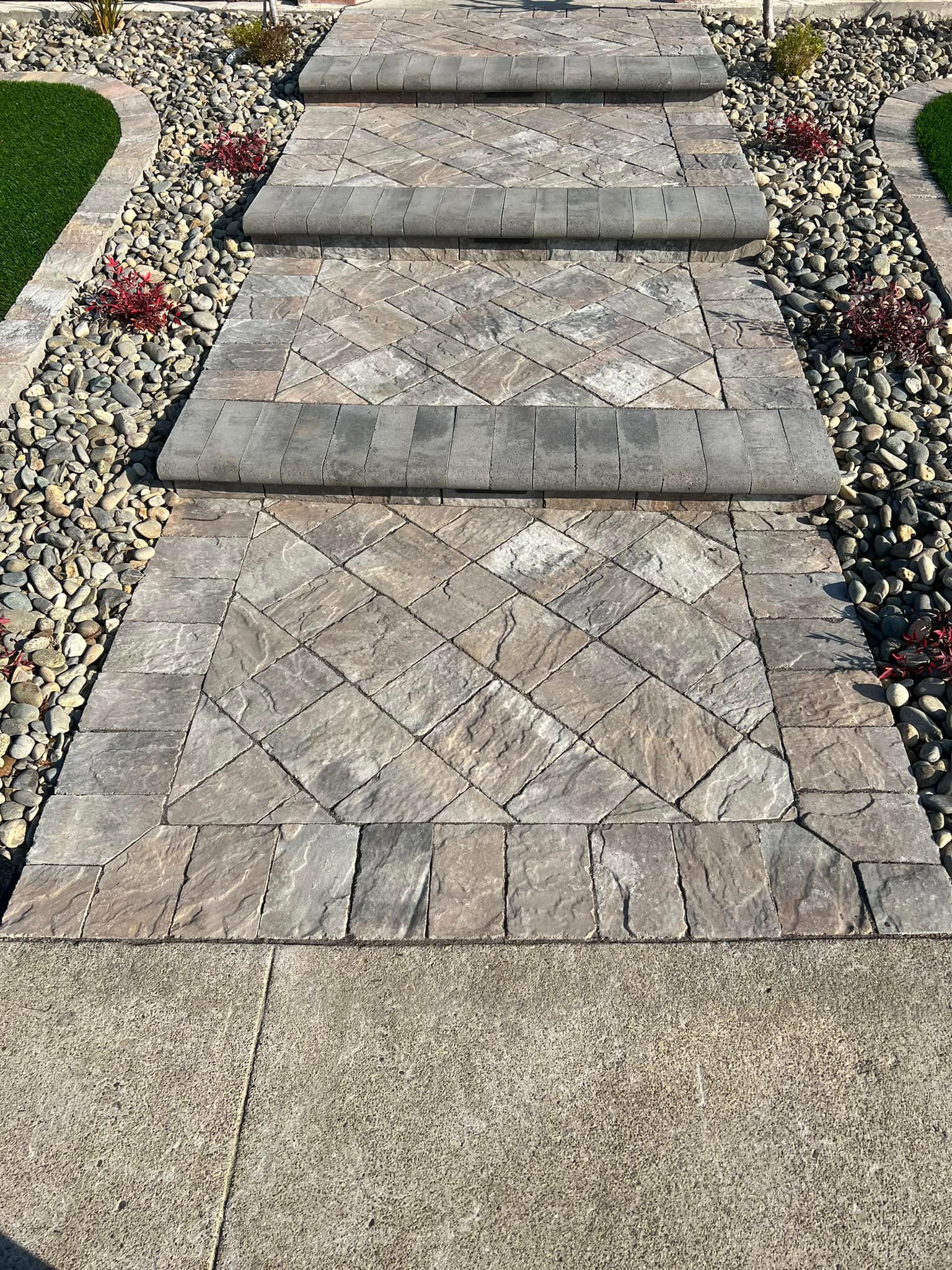 Stone steps leading up to a walkway, flanked by rocks, grass, and red plants.