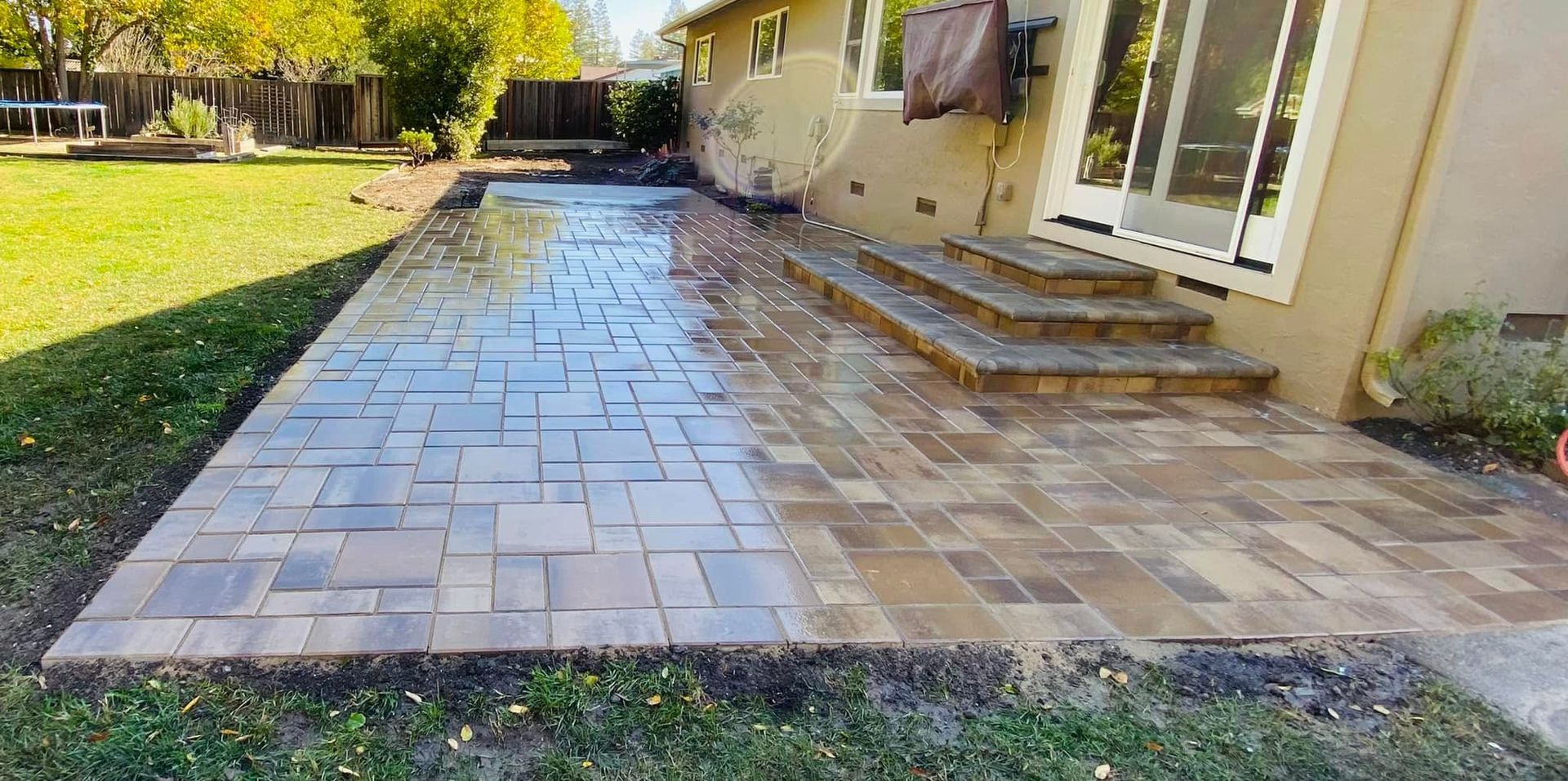 Brick patio and steps in a backyard, adjacent to a house with a sliding door.