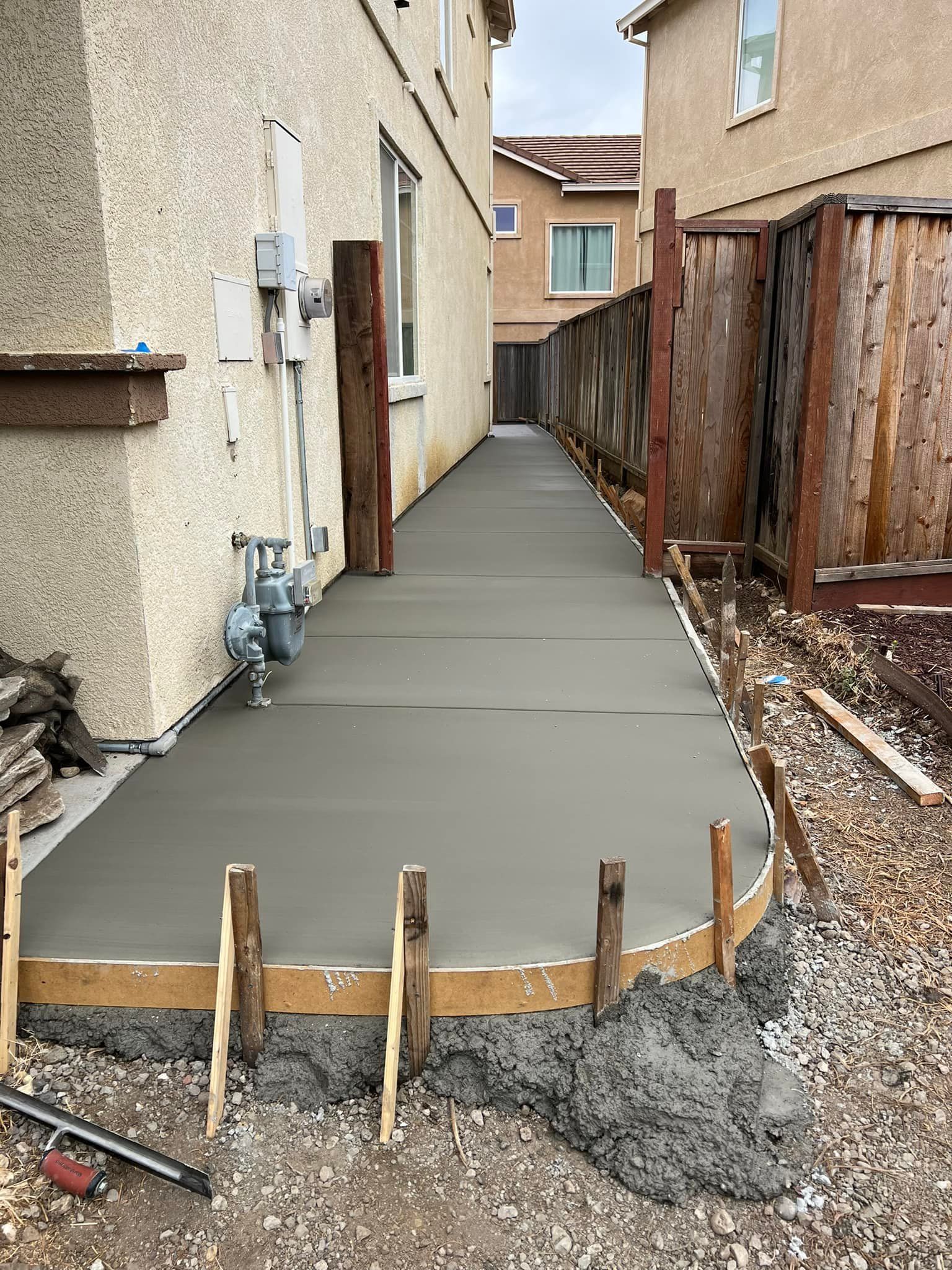 Newly poured concrete pathway between two houses, with wood framing in foreground.