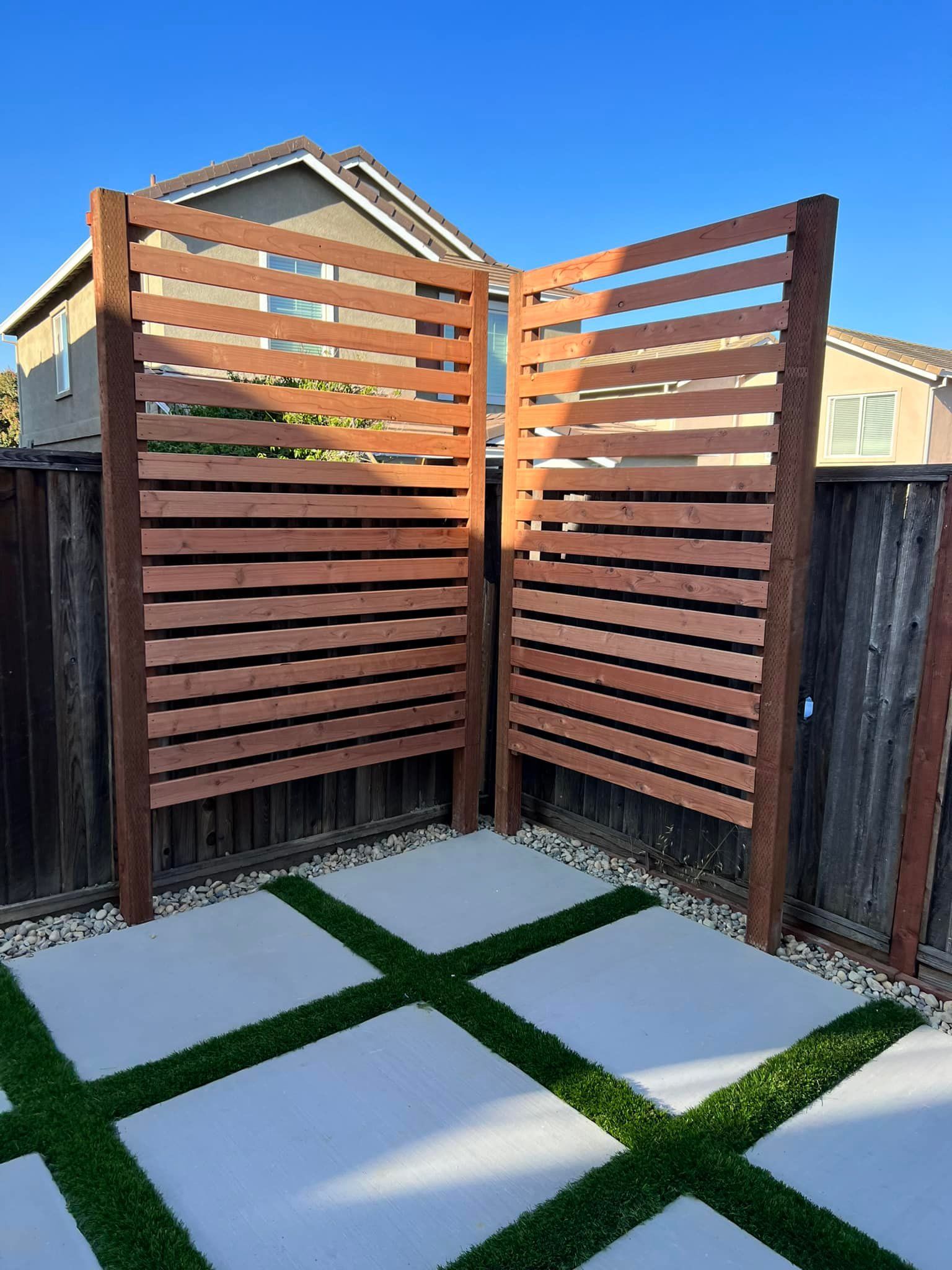 Wooden slat privacy screens in a backyard with concrete pavers and artificial grass.