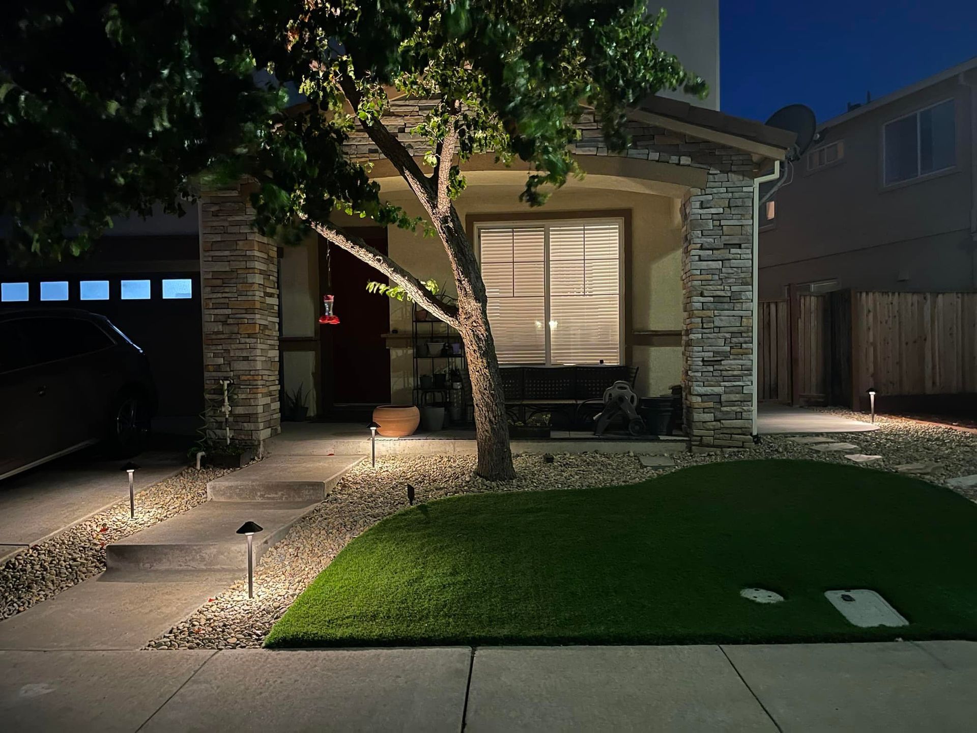 House lit up at night with lawn and stone accents. Tree in front.