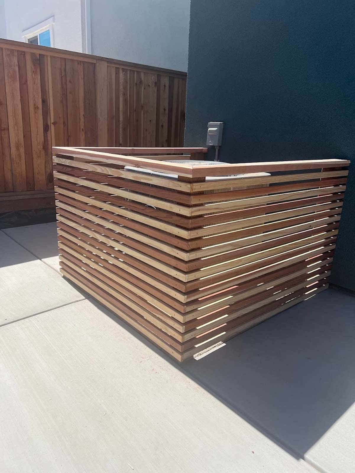Wooden planter box on a patio, brown and tan horizontal slats, next to a wooden fence.