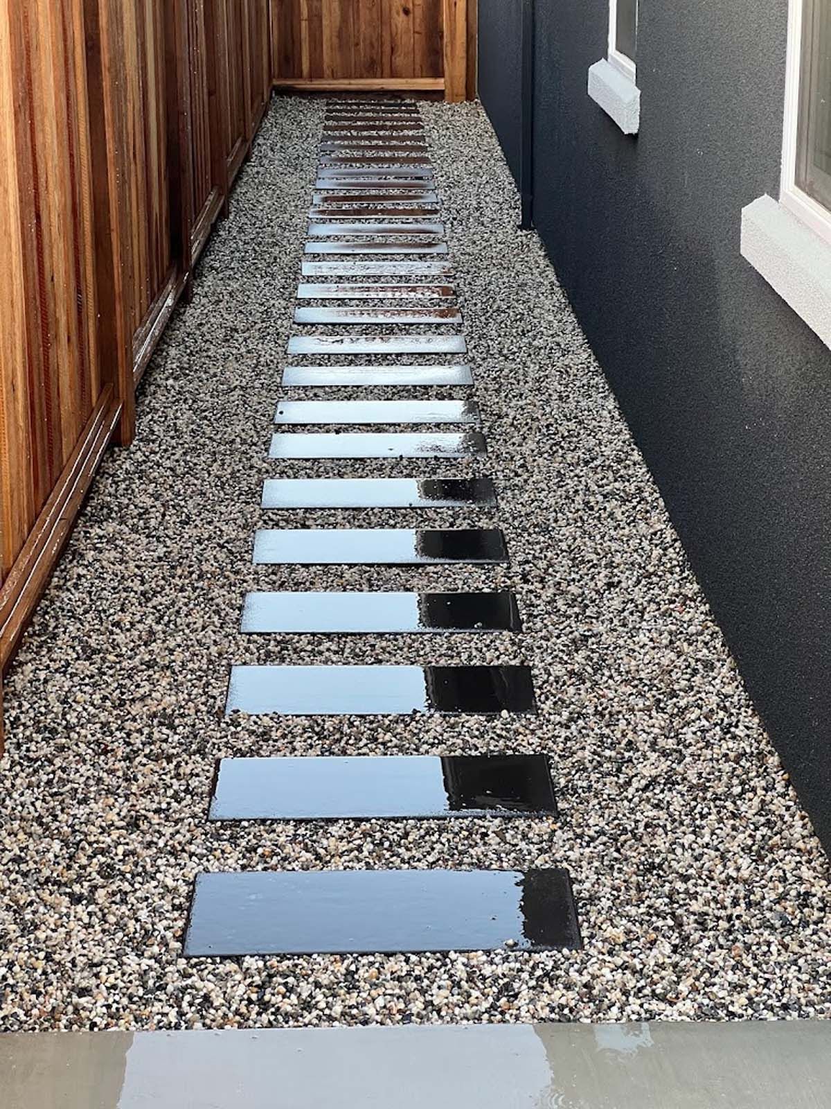 Stepping stones path through gravel between a wooden fence and a dark wall.