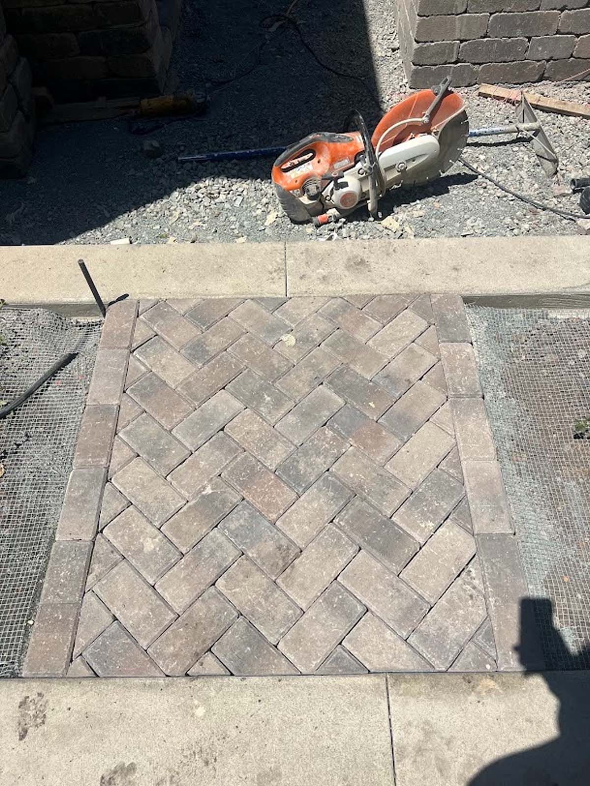 Brick pathway with herringbone pattern being constructed. A power saw sits nearby.