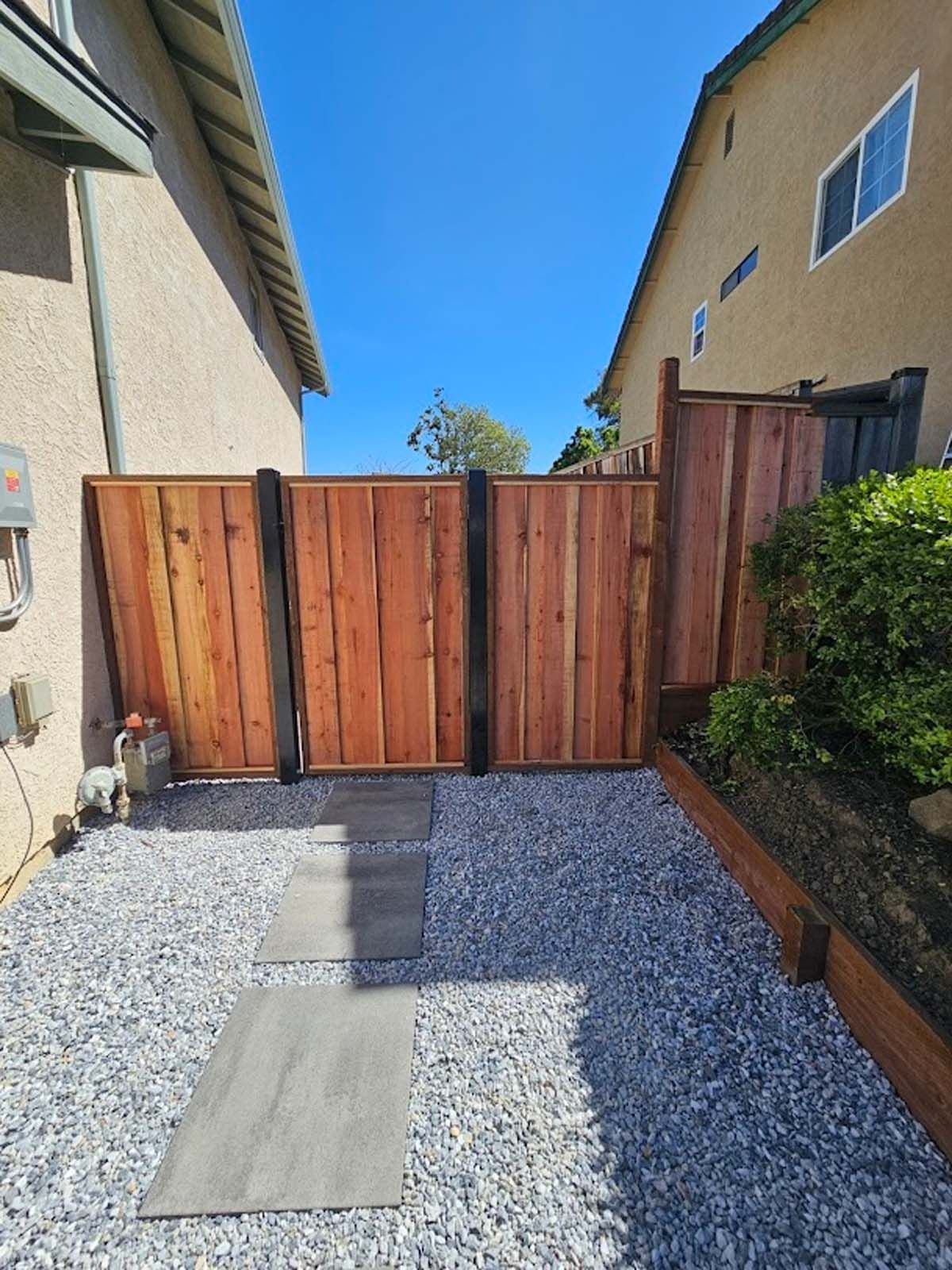 Wooden gate between two houses, leading to a gravel pathway with stepping stones.