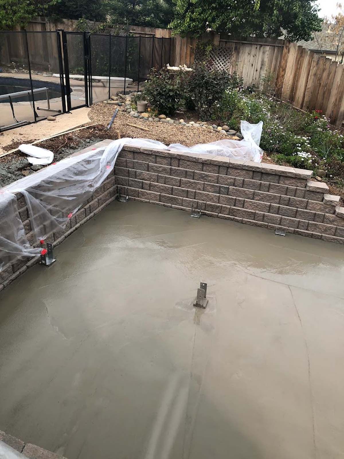 Newly poured concrete in a rectangular pit, surrounded by brick walls, in a backyard.