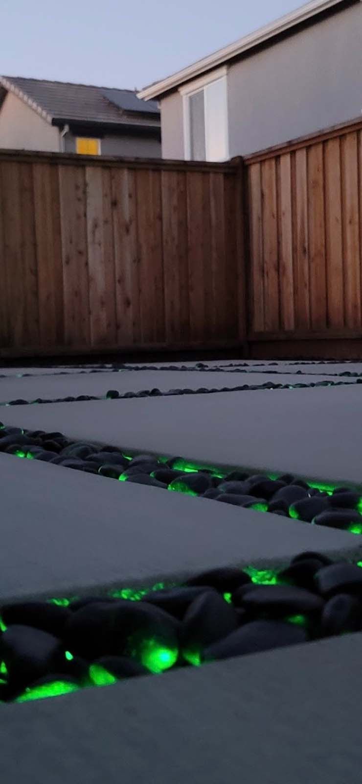 Glowing green pebbles in a patio border, next to a wooden fence.