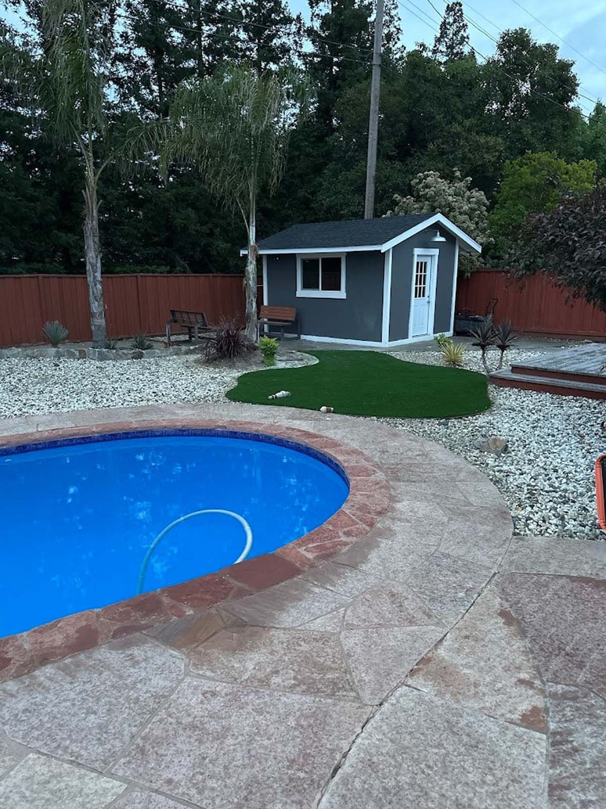 Poolside backyard with a blue pool, small gray shed, and artificial grass.