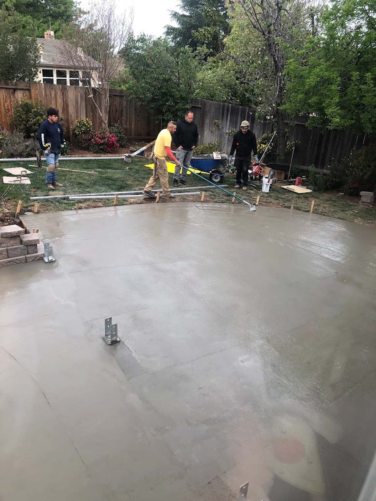 Construction workers leveling wet concrete for a patio in a backyard.