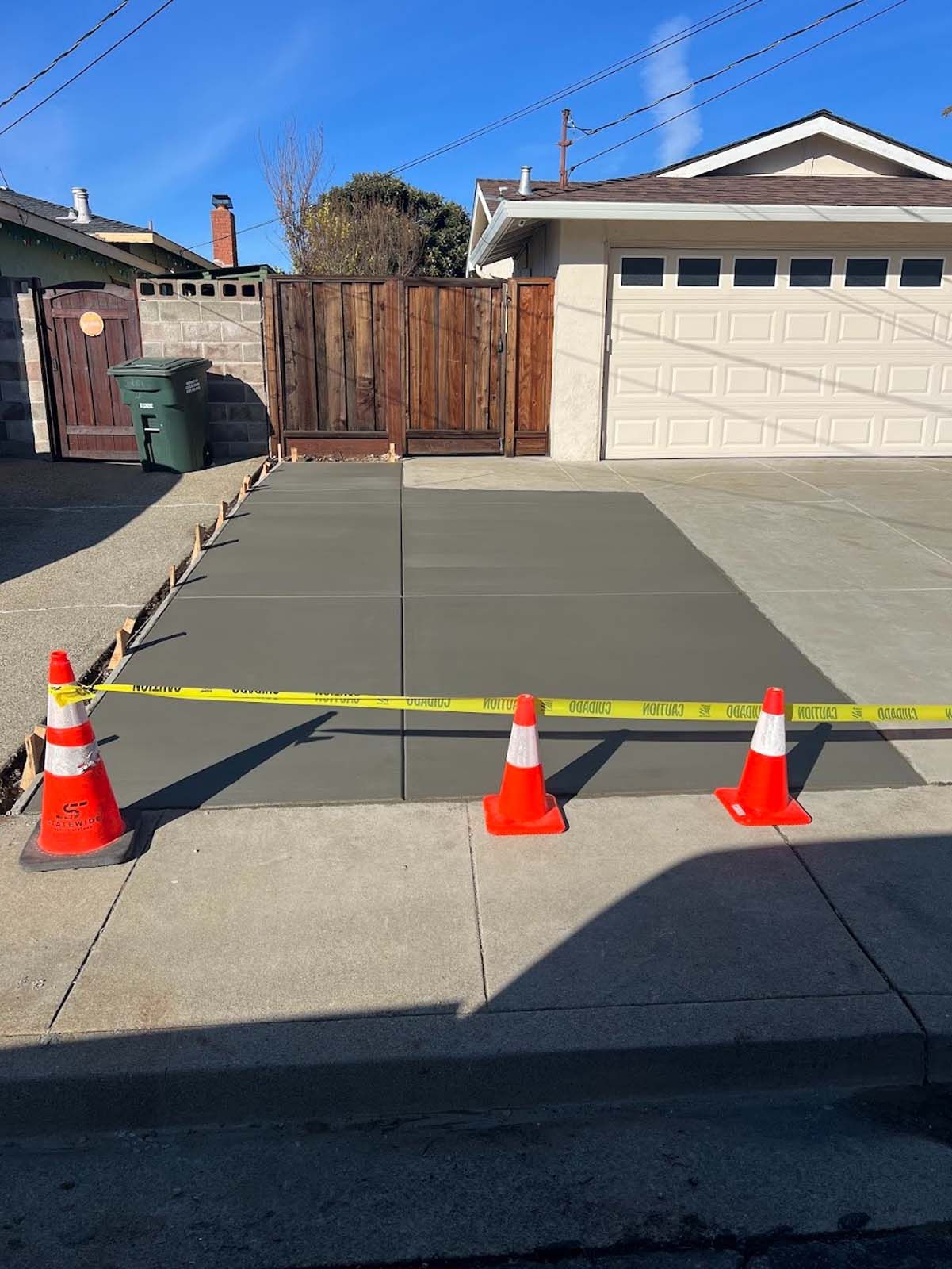 Freshly poured concrete driveway with orange safety cones and caution tape, blocking access.