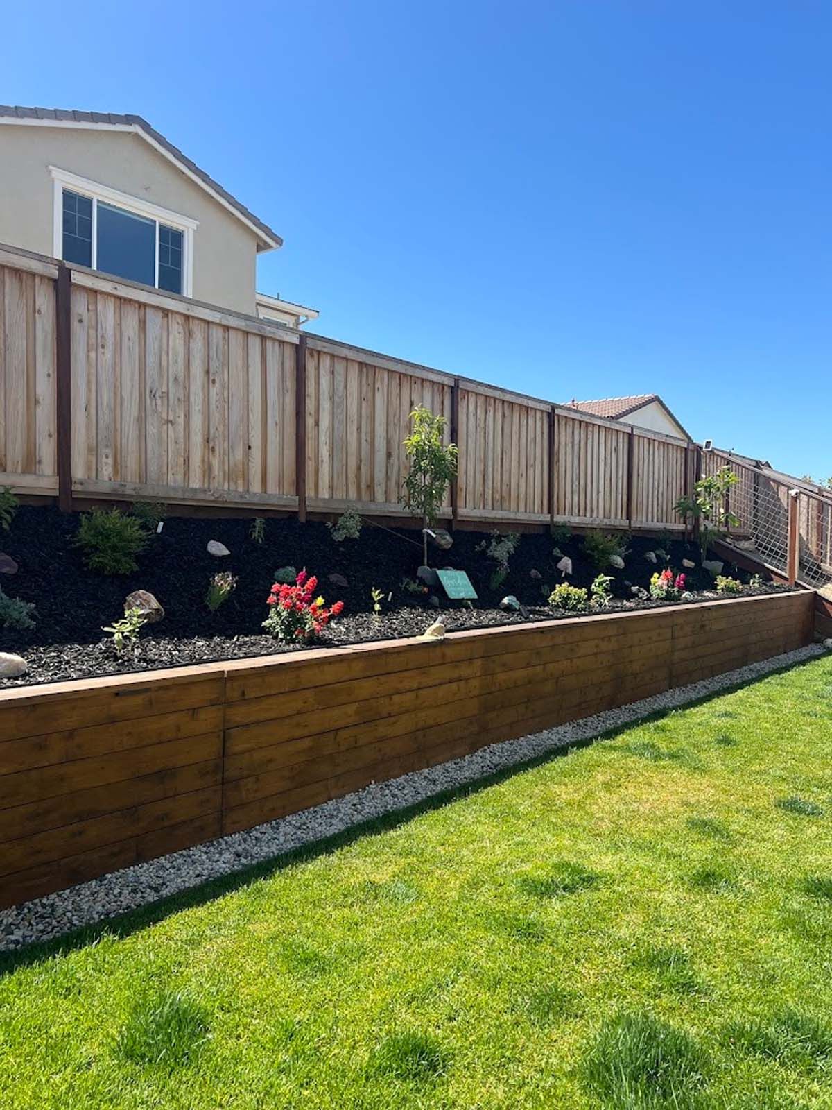 Wooden fence and retaining wall with a planted garden in a sunny backyard.