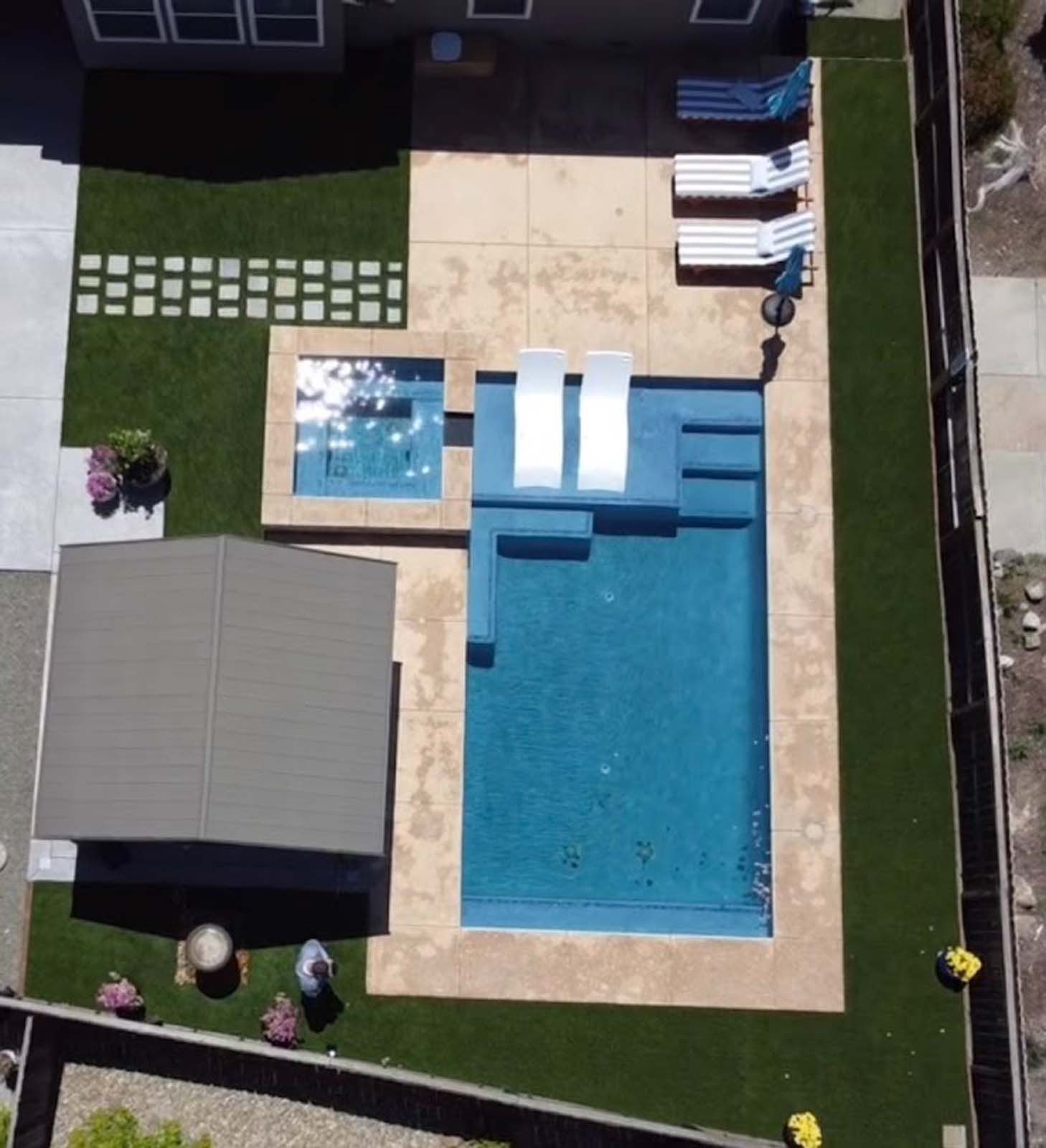 Overhead view of a backyard with a pool, hot tub, patio, and green lawn.