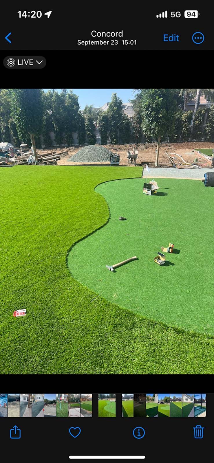 A putting green under construction, set in a grassy yard. Trees and a blue sky are in the background.