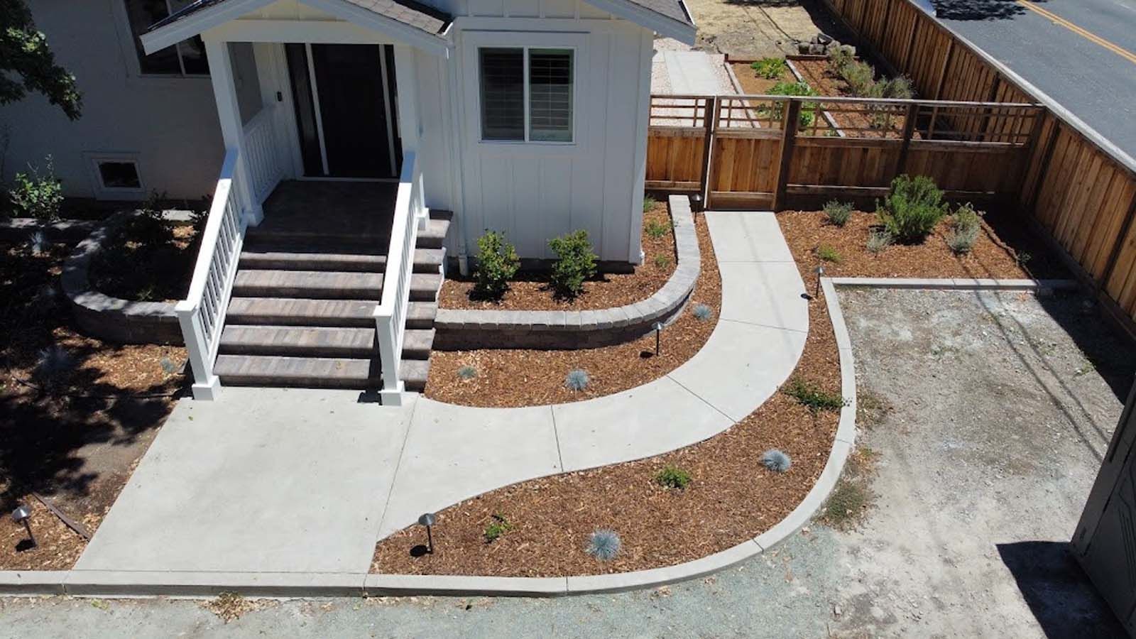 White house with concrete path and steps, bordered by brown mulch and landscaping, leading to entrance.