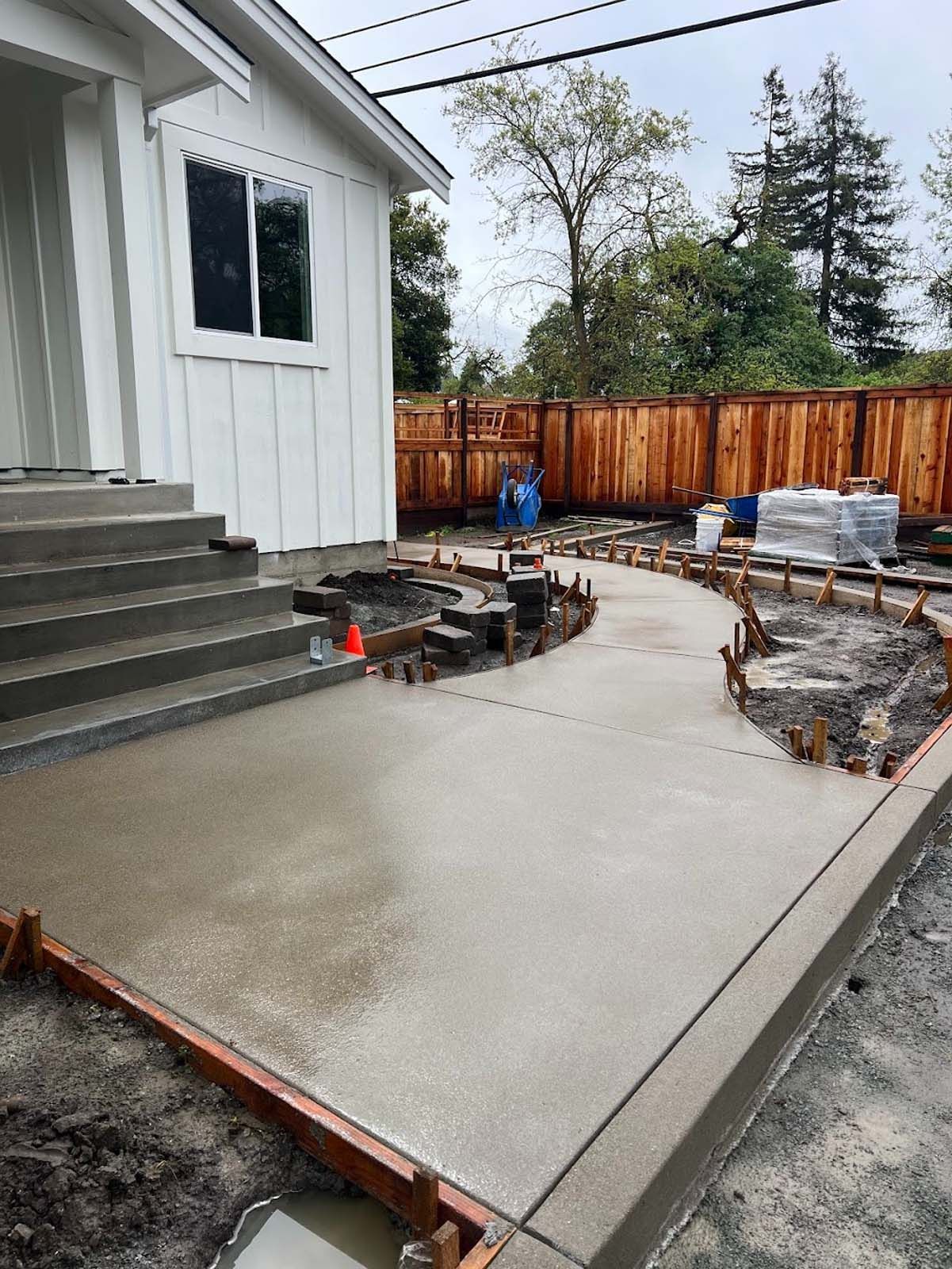 Freshly poured concrete walkway leading to a white house with wooden edging.