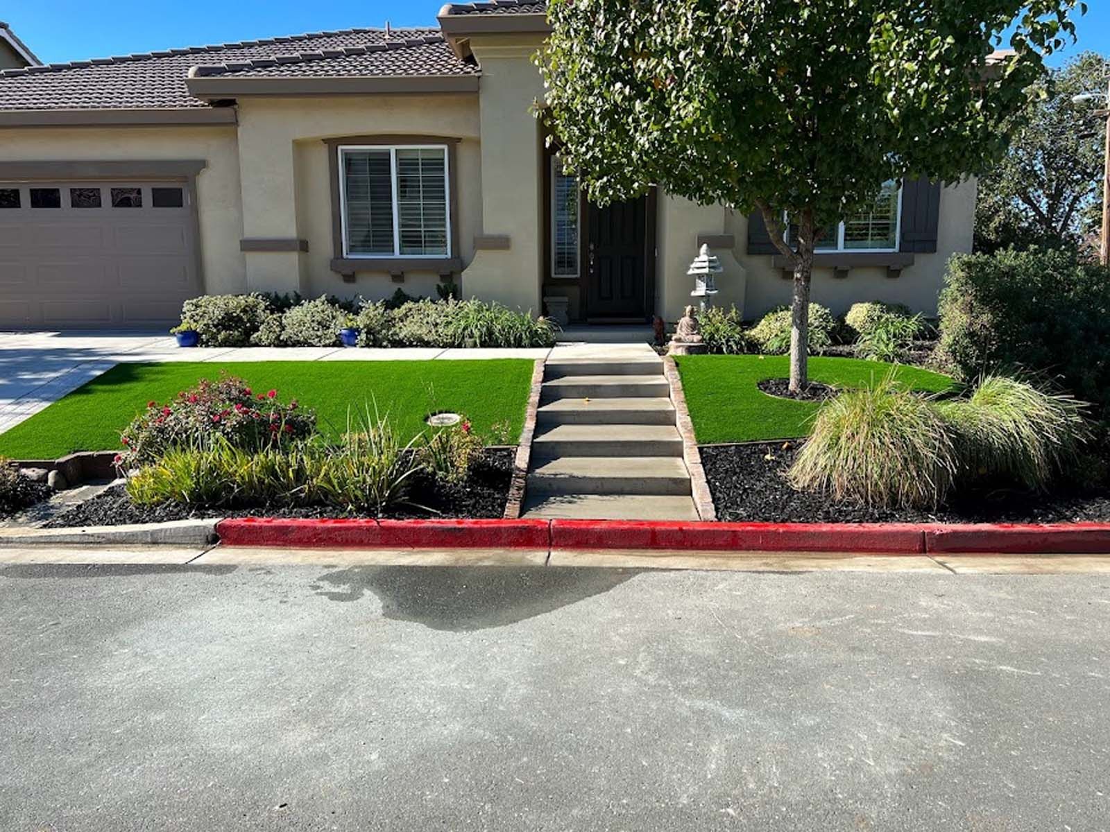 House exterior with artificial grass, landscaped beds, and steps leading to the front door.