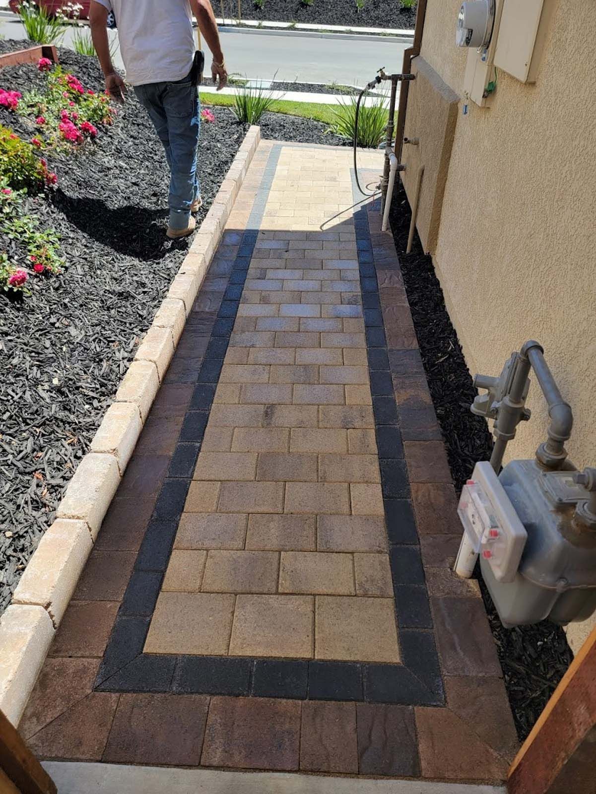Paver walkway with brick borders leading to a house, person walking on it.